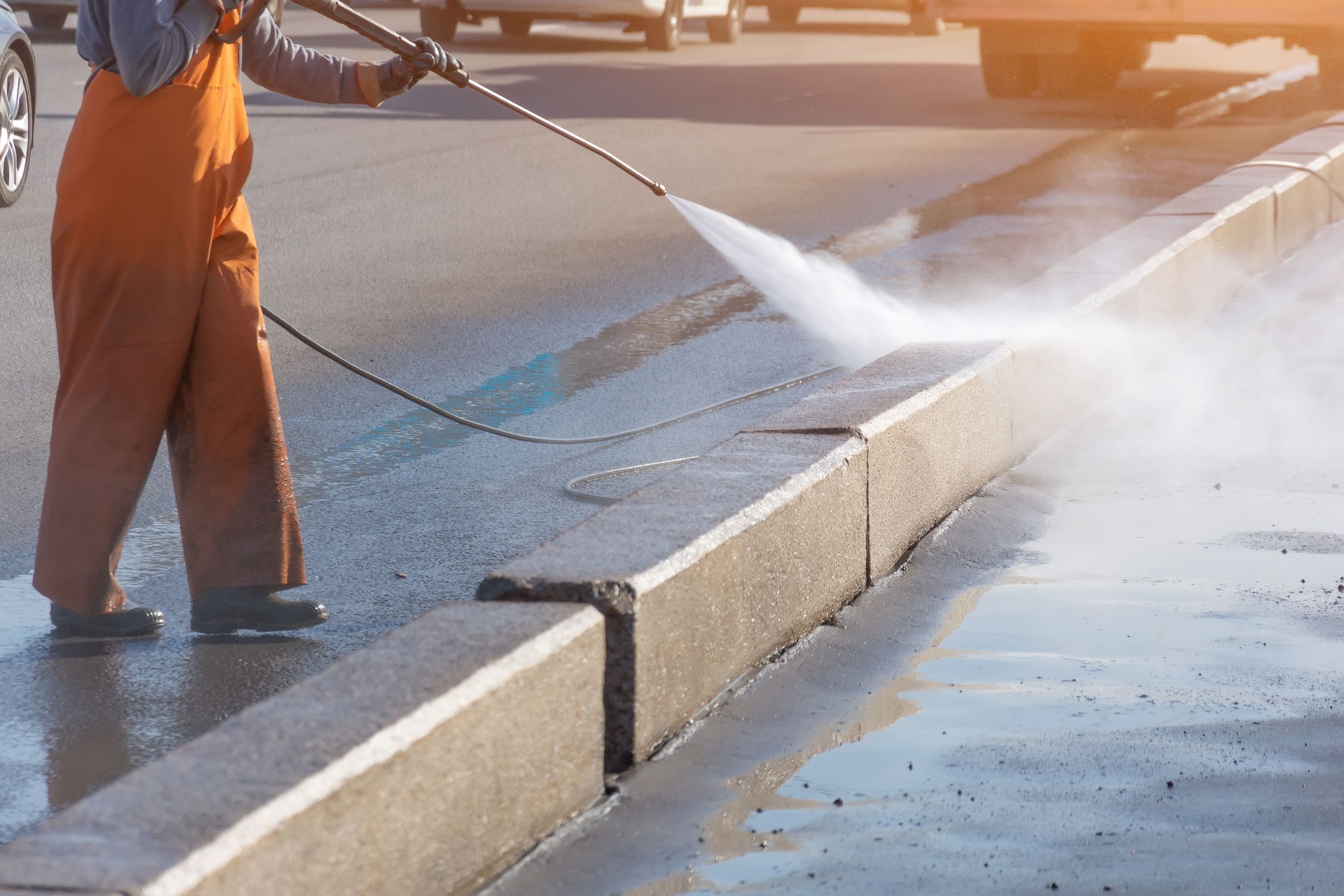 Worker cleaning driveway with gasoline high pressure washer splashing the dirt, asphalt road border. High pressure cleaning.
